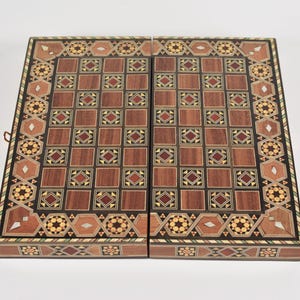 Könnte beinhalten: Ein rechteckiges Backgammon-Spielbrett aus Holz mit aufwendiger Intarsienarbeit und geometrischen Mustern in Braun-, Beige- und Cremetönen. Die Oberfläche zeigt ein Raster aus Quadraten mit eingelegten Stern- und Rautenmotiven.