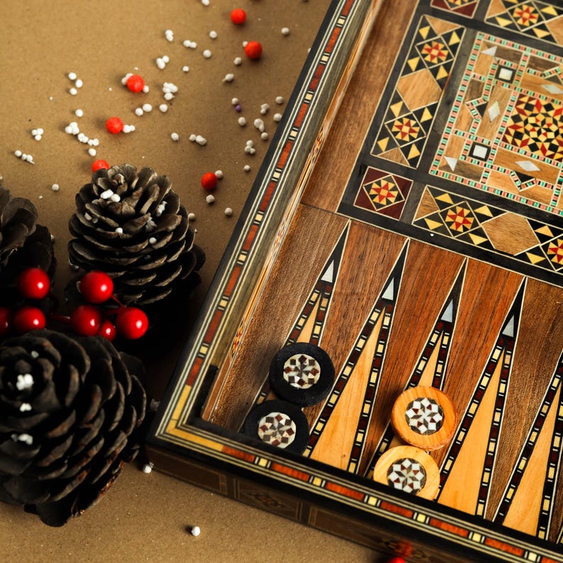 May include: A wooden backgammon board with intricate inlaid designs in shades of brown, black, and white. The board is set up for play with black and white game pieces.