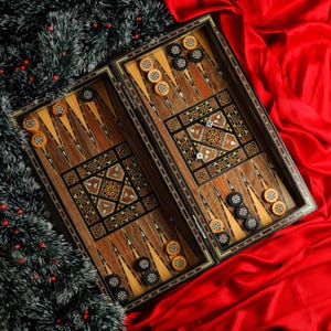 May include: A wooden backgammon set with intricate inlaid designs. The board is open and shows the playing pieces, which are black and white. The board is on a red fabric surface.