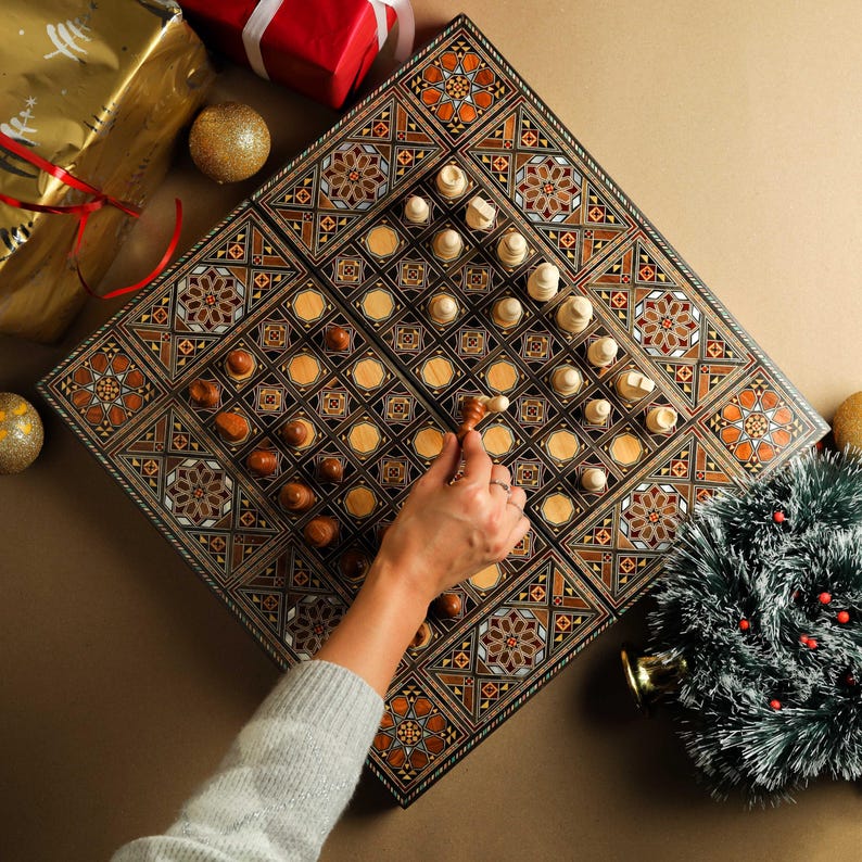 May include: A wooden game board with intricate inlaid designs in shades of brown, gold, and white. The board features a chessboard on one side and a backgammon board on the other. A hand is shown moving a chess piece on the board.