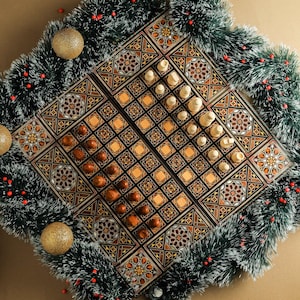 May include: A wooden chess and draughts set with intricate inlaid designs. The board is decorated with geometric patterns in shades of brown, gold, and black. The pieces are made of wood and are arranged on the board in a game in progress.