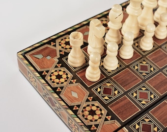 Könnte beinhalten: Ein Schachspiel aus Holz mit einem Brett, das komplexe geometrische Intarsien in Braun-, Schwarz- und Cremetönen aufweist, akzentuiert durch Perlmutt-Einlagen. Das Brett ist mit hellen, geschnitzten Schachfiguren aus Holz, darunter Bauern, besetzt.