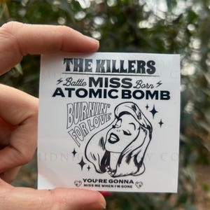 May include: Black and white sticker featuring a cartoon woman with the text "The Killers Battle Miss Born Atomic Bomb Burnin' For Love You're Gonna Miss Me When I'm Gone"