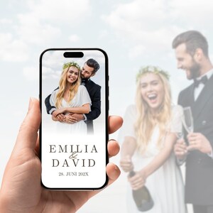 May include: A smartphone screen displaying a wedding photograph of a couple, with the text EMILIA & DAVID and the date 28. JUNI 202X printed below the image in a dark serif font against a clean white background.
