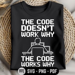 Può includere: Maglietta nera con testo bianco che recita "The code doesn't work why the code works why". Il testo è in un font pixelato. C'è una piccola illustrazione di una persona seduta davanti a un computer.