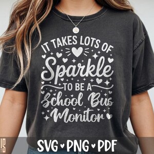 May include: A charcoal grey short-sleeve t-shirt featuring white text that reads IT TAKES LOTS OF Sparkle TO BE A School Bus Monitor. The design includes various white heart and star icons surrounding the text, printed on the front of the shirt.