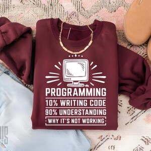 May include: A maroon sweatshirt with a white graphic print that reads "PROGRAMMING 10% WRITING CODE 90% UNDERSTANDING : WHY IT'S NOT WORKING:" and a stylized image of a computer monitor.