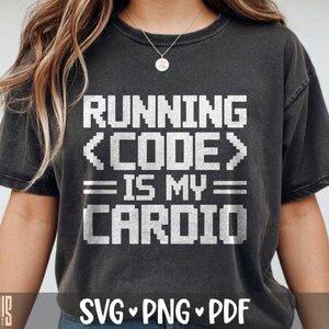May include: A charcoal gray short-sleeve t-shirt featuring white pixelated text that reads RUNNING <CODE> IS MY CARDIO. The design is centered on the chest, and the fabric has a slightly faded, vintage-inspired appearance with a crew neckline.