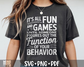 May include: A charcoal gray short-sleeve t-shirt featuring white text that reads: IT'S ALL FUN AND GAMES UNTIL SOMEONE FIGURES OUT THE FUNCTION OF YOUR BEHAVIOR. The shirt has a crew neckline and a distressed, washed-out fabric appearance.