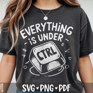 May include: A charcoal gray short-sleeve t-shirt featuring a white graphic of a computer keyboard control key. The text above the key reads Everything is under CTRL in a distressed white font. The design includes small decorative white marks.