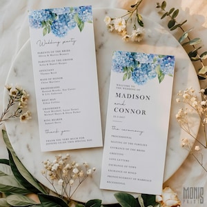 Pode incluir: Dois programas de cerimónia de casamento com design floral de hortênsias azuis. Os programas listam os detalhes da cerimónia e os nomes dos noivos. Os programas estão numa superfície de mármore branco.