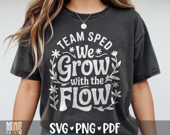 May include: A charcoal gray short-sleeve t-shirt featuring white text that reads TEAM SPED We Grow with the FLOW, surrounded by a decorative floral vine graphic. The design is printed in a distressed white font on the front of the garment.