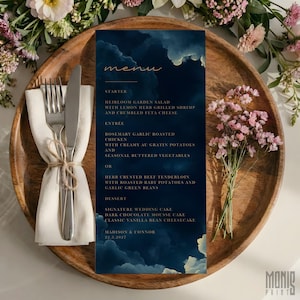 May include: A wedding menu card with a dark blue background and a cloud-like design. The menu includes starters, entrees, and desserts. The card is on a wooden tray with a napkin, silverware, and flowers.