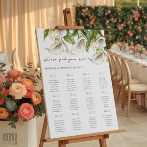 Pode incluir: Um quadro branco de disposição de mesas de casamento num cavalete de madeira, com uma ilustração em aguarela de lírios calla brancos no topo. O texto diz "please find your seat", "MADISON & CONNOR | 22.3.2027" e lista os nomes dos convidados.