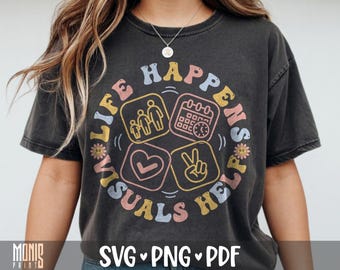 May include: A charcoal gray short-sleeve t-shirt featuring a circular graphic with the text "LIFE HAPPENS VISUALS HELP". The design includes four square icons depicting a family, a calendar with a clock, a heart, and a peace sign, with small flowers.