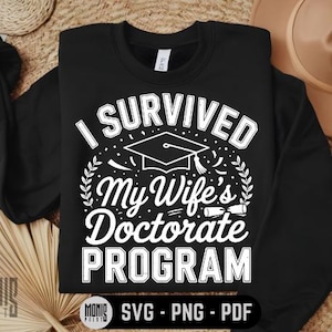 May include: Black sweatshirt with white text that reads "I Survived My Wife's Doctorate Program". The text is surrounded by a graduation cap, stars, and confetti.