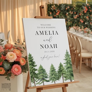 May include: A white wedding welcome sign on a wooden easel. The sign reads "Welcome to our wedding" above the names "Amelia and Noah" and the date "29.11.2026". Green watercolor pine trees are at the bottom.