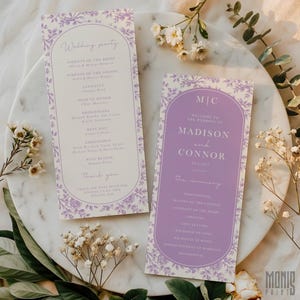 May include: Two wedding ceremony programs with a floral design in lavender and white. The programs include the wedding party details and ceremony order. The programs are on a marble surface with floral accents.