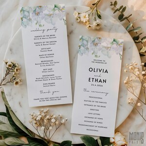 Könnte beinhalten: Zwei Hochzeitskarten mit floralen Akzenten. Die Karten zeigen die Namen Olivia und Ethan, das Datum 24.4.2026 und die Details der Hochzeitsgesellschaft. Das Design umfasst einen zarten floralen Rand in Weiß- und Grüntönen.