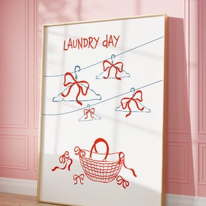 May include: A white framed print with the text "LAUNDRY DAY" in red. The print features a red wicker basket and red bows on blue clothes hangers.