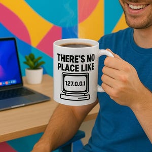 Könnte beinhalten: Eine weiße Kaffeetasse mit schwarzem Text, der "There's no place like 127.0.0.1" lautet, mit einem Computermonitor-Symbol.