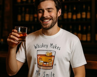 Könnte beinhalten: Ein weißes T-Shirt mit einer Cartoon-Illustration eines Glases Whisky mit einem lächelnden Gesicht. Der Text "Whiskey Makes Me Smile" ist auf das Shirt gedruckt.