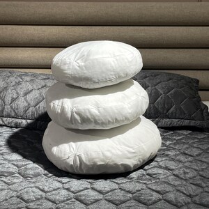 May include: Three white round pillows stacked on top of each other on a gray quilted bedspread.