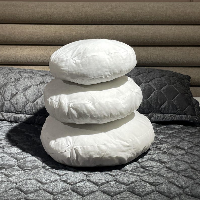 May include: Three white round pillows stacked on top of each other on a gray quilted bedspread.
