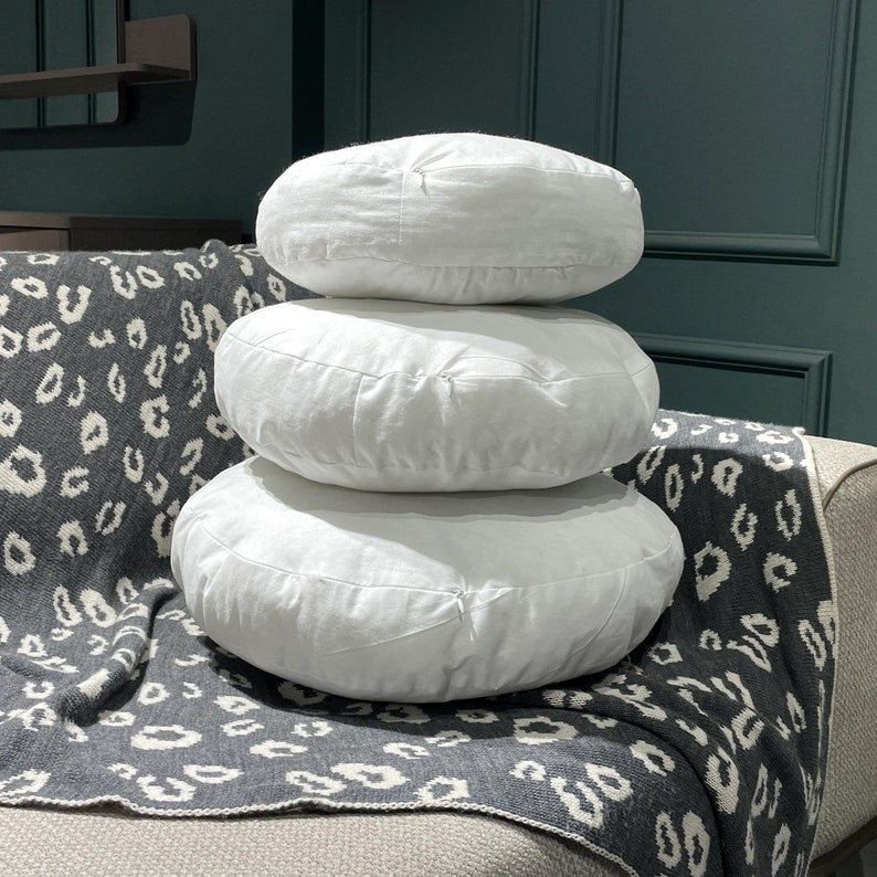 May include: Three white round cushions stacked on top of each other on a gray and white patterned throw blanket.