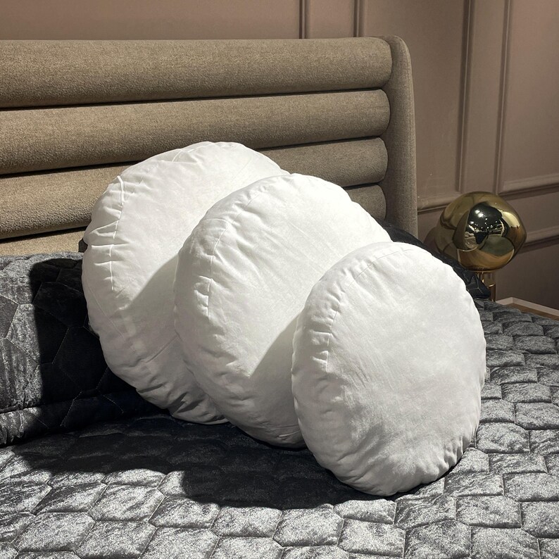 May include: Three white round pillows of different sizes on a black and gray patterned bed.