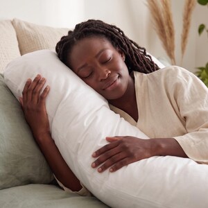 May include: A long, white body pillow with a smooth fabric cover. The pillow is rectangular in shape and designed to support the full length of the body while resting. It features a clean, plain white surface without any patterns or textures.