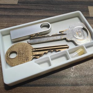 May include: A white rectangular tray with compartments holds a silver USB drive, two keys, and a capsule. One key is gold with the text "COUNTY LOCKSMITHS SECURITY". The other key is silver with the "YALE" logo.