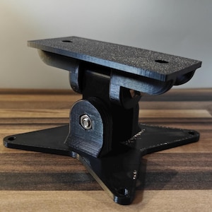 May include: A black, adjustable bracket with a textured top surface and a star-shaped base. The bracket has a pivoting design and is secured with a bolt. The product is designed to hold an object.