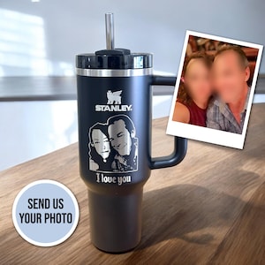 May include: A black stainless steel travel mug with a handle and a straw. The mug has a personalized engraving of a couple and the words "I love you". The mug also has the Stanley logo and a small bird logo.