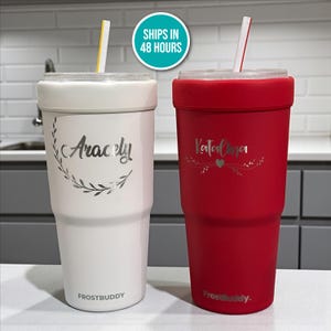 May include: Two personalized FrostBuddy tumblers. One is white with the name "Aracely" and a leaf design, the other is red with "Katalina" and a heart design. Both have straws and clear lids.