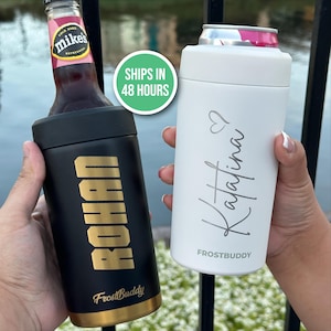 May include: Two insulated beverage holders, one black with gold lettering reading "ROHAN" and the other white with the name "Katalina" in silver script. Both holders are designed to keep drinks cold. The black holder holds a bottle, and the white one holds a can.