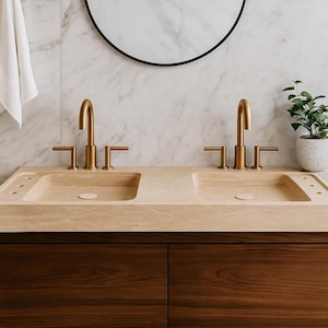 Peut inclure: Un meuble-lavabo de salle de bain moderne avec deux éviers et des robinets dorés. Les éviers sont intégrés dans un comptoir beige clair, au-dessus de meubles en bois brun foncé. Un mur à motifs de marbre et un miroir noir rond complètent le design.