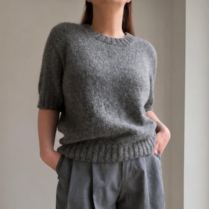 May include: A charcoal gray short-sleeved sweater with a ribbed crew neckline and hem, paired with loose-fitting gray trousers featuring front pleats. The sweater has a fuzzy, textured knit appearance, while the trousers have a smooth finish.