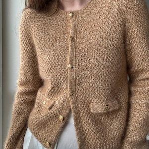Peut inclure: Un cardigan marron avec des boutons dorés et deux poches. Le cardigan est fait d'un matériau doux et duveteux.