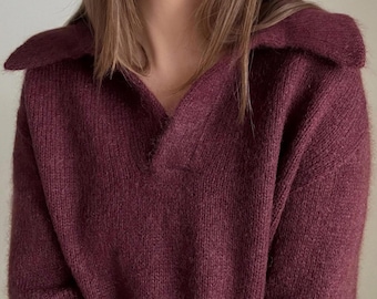 May include: A burgundy knitted sweater with a v-neck and a collar. The sweater is made of a soft, fuzzy material.