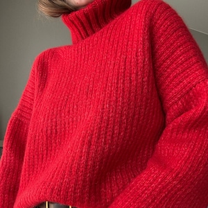 Könnte beinhalten: Ein roter Rollkragenpullover mit gerippter Struktur. Der Pullover ist aus weichem, flauschigem Material und hat eine lockere Passform.