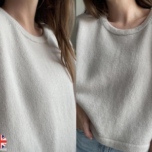 Op de afbeelding: Een licht beige gebreide trui met een ronde hals en korte mouwen.