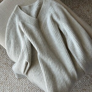 May include: A light gray knitted sweater with a V-neck and long sleeves.