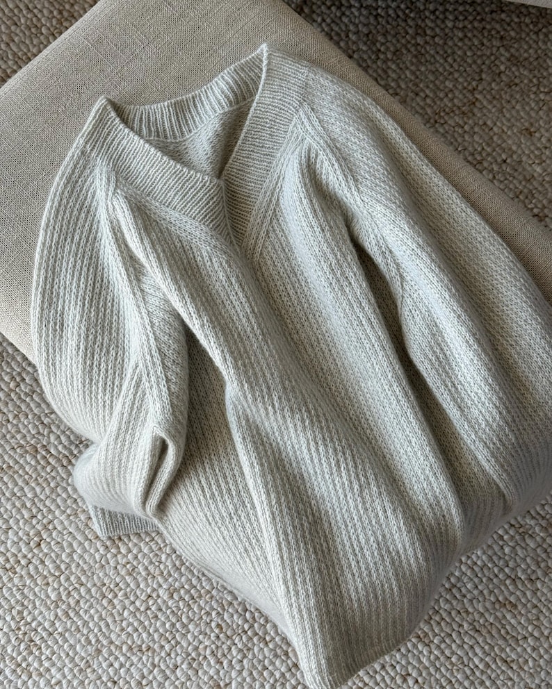 May include: A light gray knitted sweater with a V-neck and long sleeves.