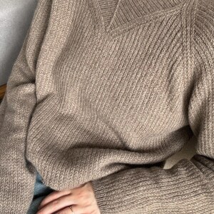 May include: A brown knitted sweater with a V-neck and long sleeves. The sweater is made of a soft, comfortable material and has a relaxed fit.
