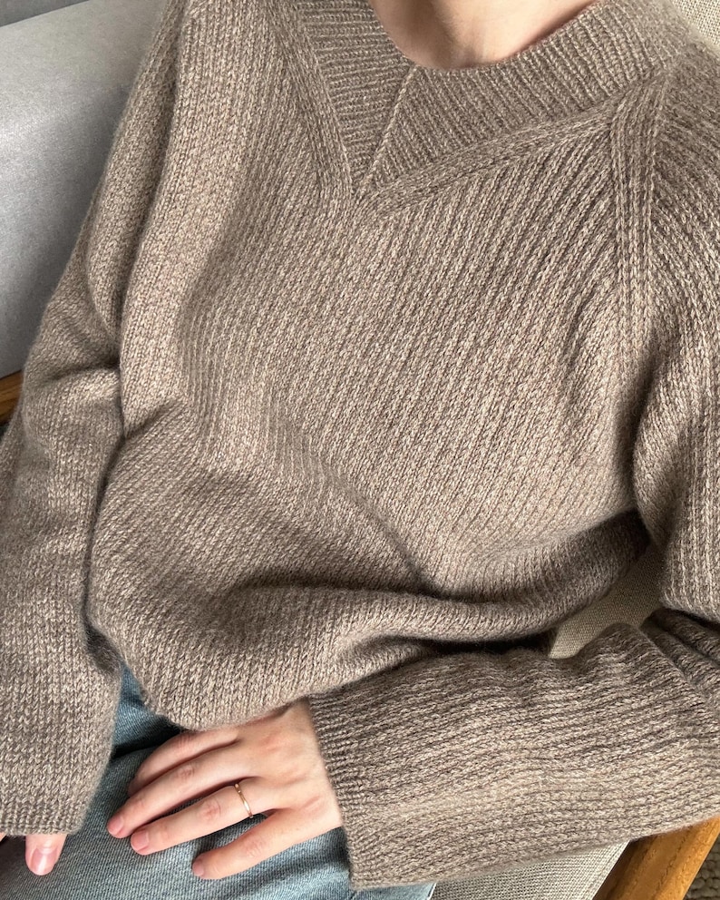 May include: A brown knitted sweater with a V-neck and long sleeves. The sweater is made of a soft, comfortable material and has a relaxed fit.