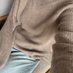 May include: A brown knitted sweater with a v-neck and long sleeves. The sweater is made of a soft, fuzzy material.