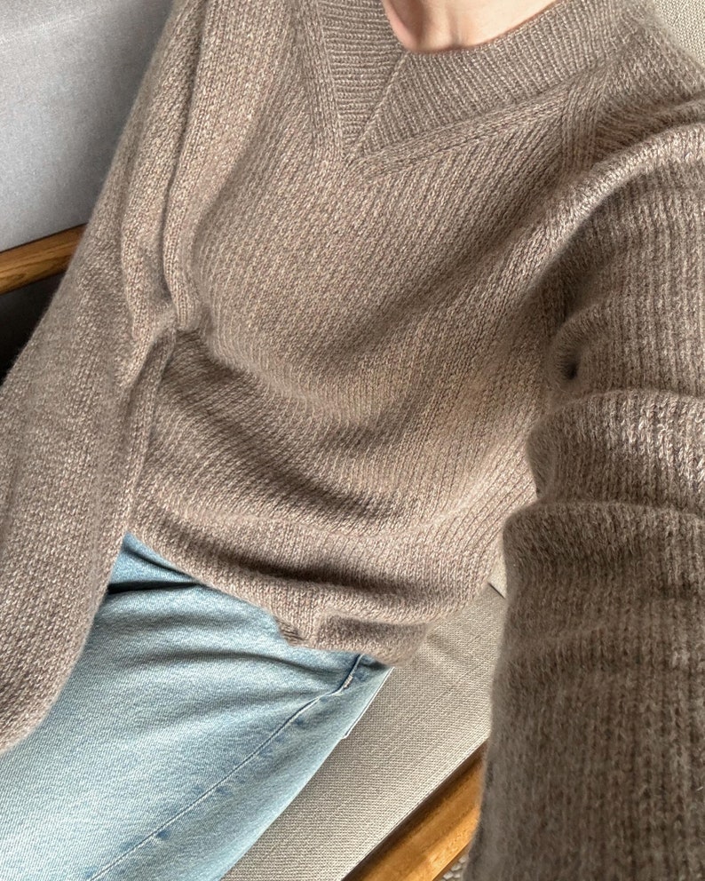May include: A brown knitted sweater with a v-neck and long sleeves. The sweater is made of a soft, fuzzy material.