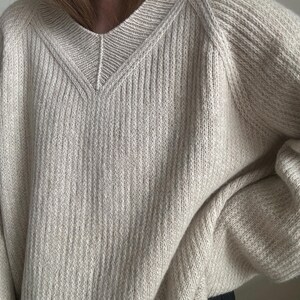 May include: A cream-colored knitted sweater with a v-neck and long sleeves.