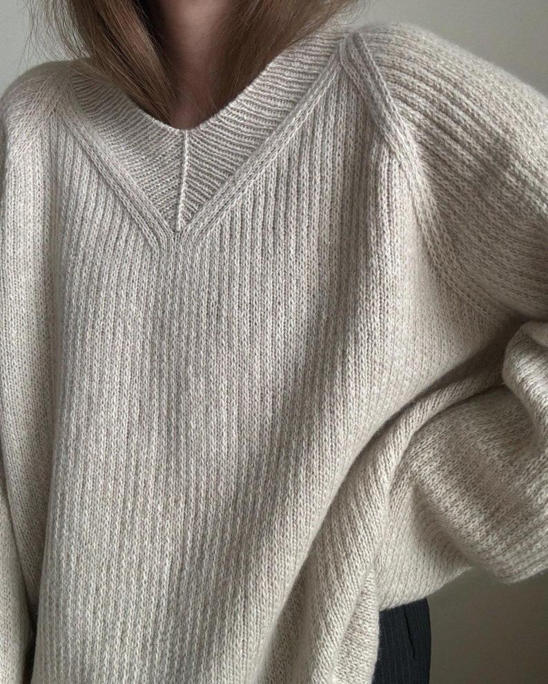May include: A cream-colored knitted sweater with a v-neck and long sleeves.